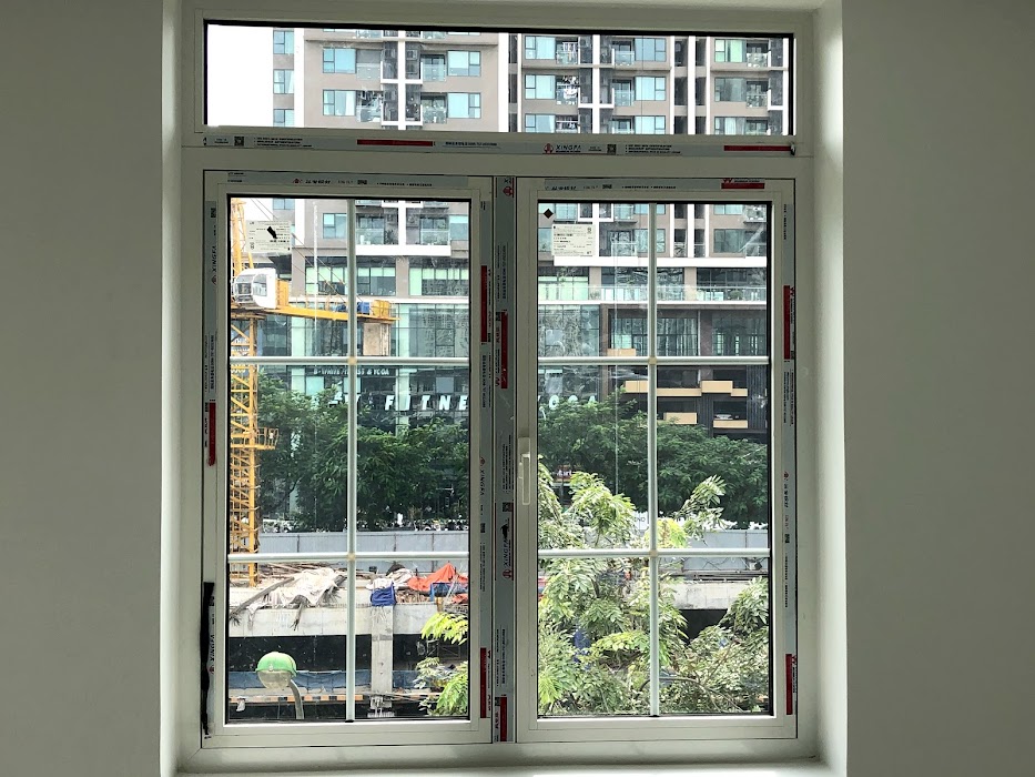 Cửa sổ nhôm kính Xingfa hai cánh đang lắp đặt trong căn hộ nhìn ra khu chung cư và cây xanh